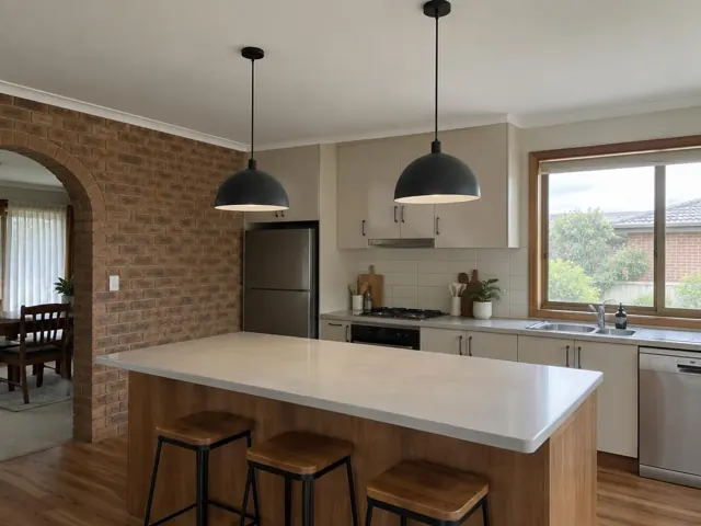 Kitchen with two black pendant lights over a light stone island, brick arch and window in Elermore Vale